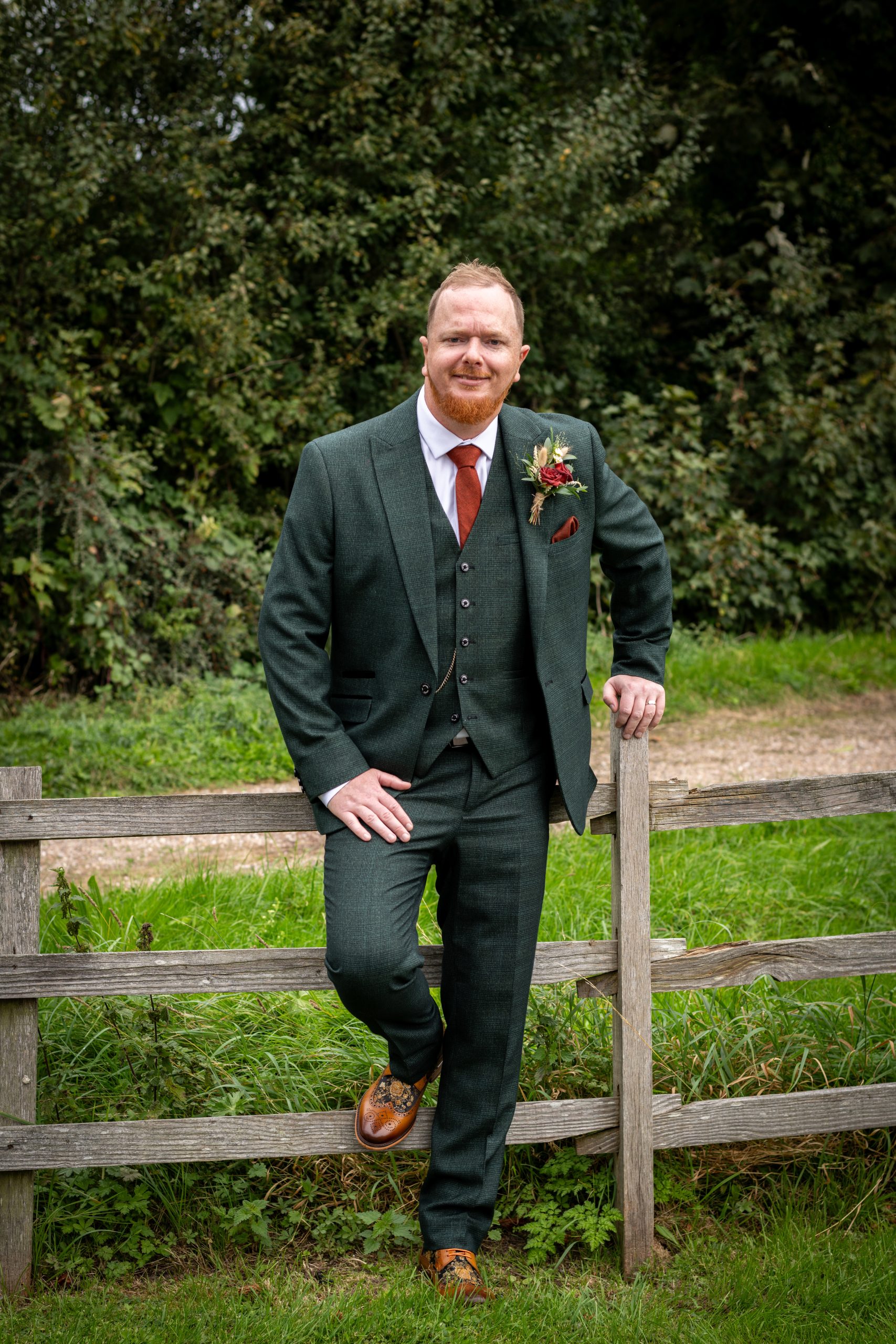 David Cadden, Mid North Coast and NSW wedding photographer, smiling in a green suit beside a wooden fence.