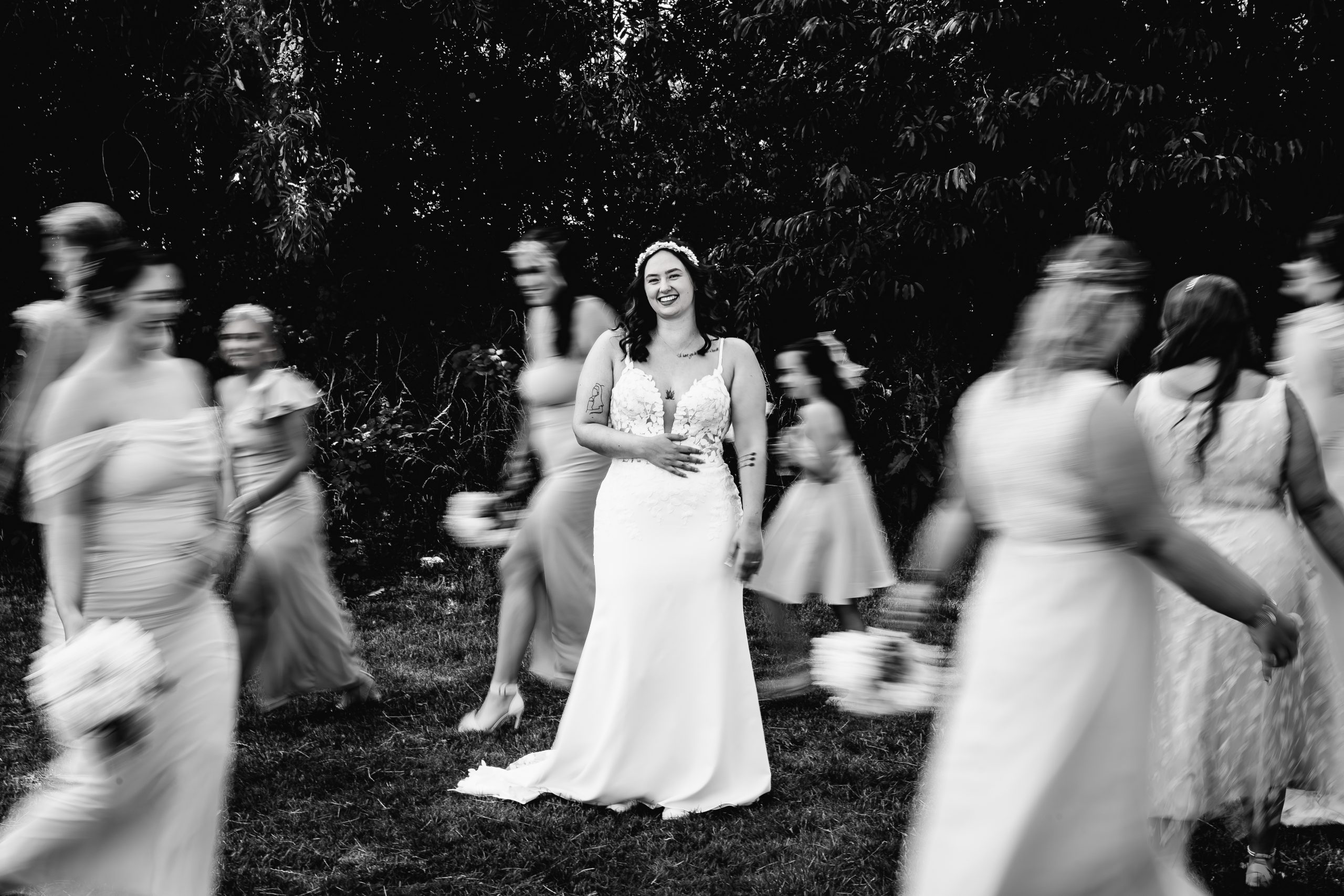 Bride smiling during wedding portraits surrounded by moving bridesmaids, photographed by David Cadden Photography