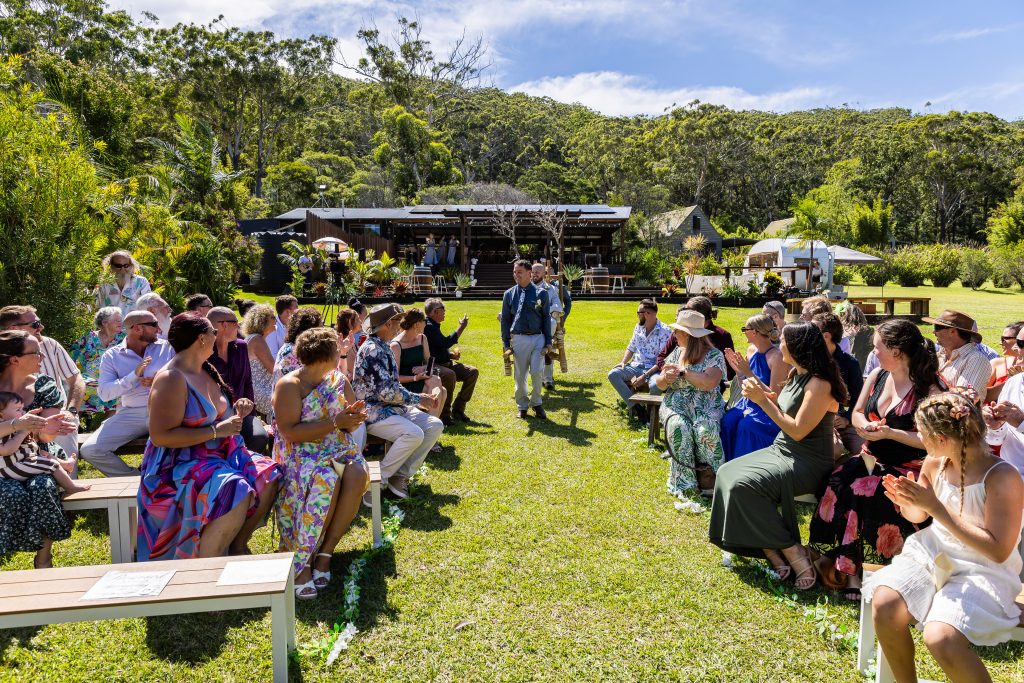 Outdoor wedding ceremony at Goolawah Bush & Beach Retreat in Crescent Head, with guests seated on the lawn and the pavilion behind.